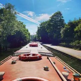 Narrowboat on a canal with trees and a blue sky with contrails.