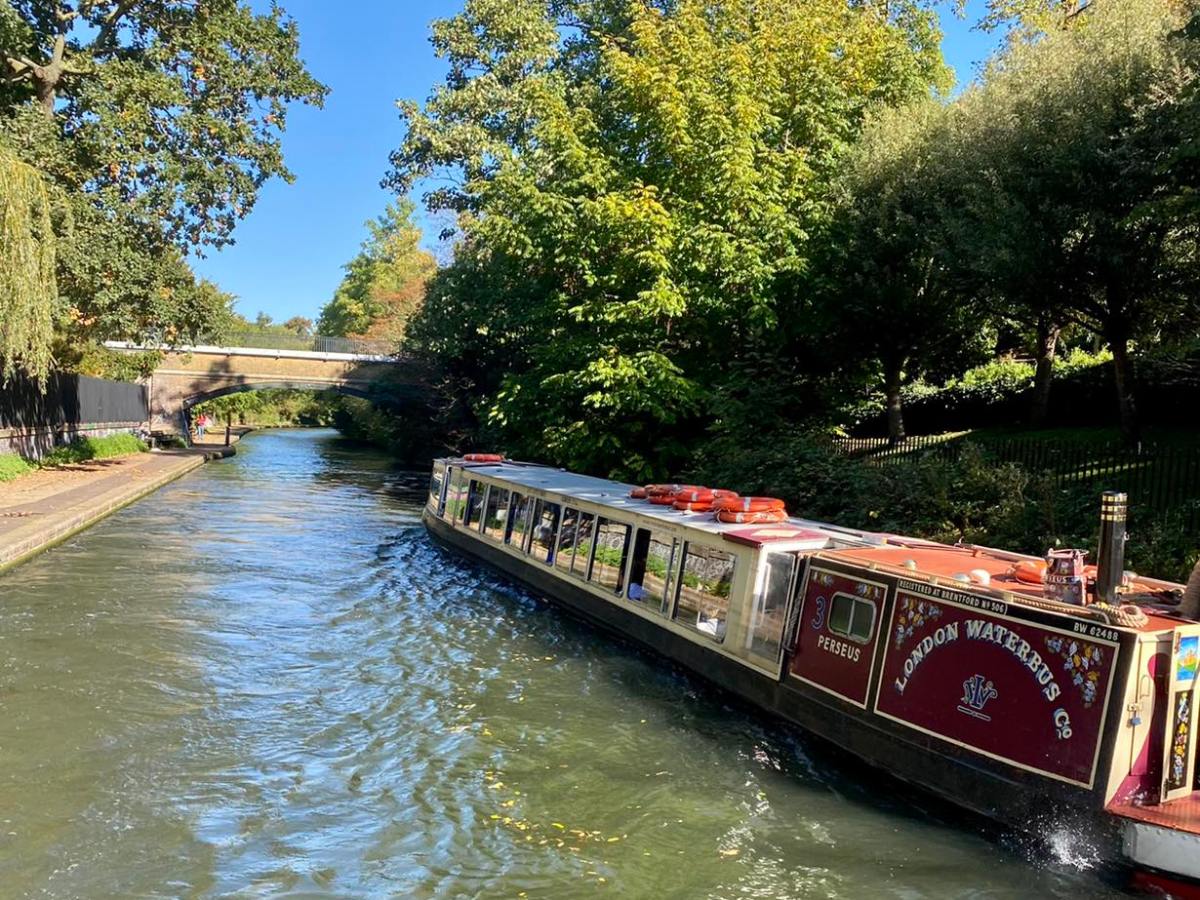 Canal boat on a tree-lined waterway under a clear blue sky.