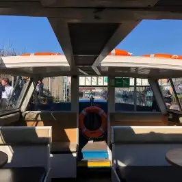 Interior view of a boat with seats, tables, a lifebuoy, and windows on a sunny day.