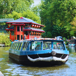 Boat on canal near red building with lanterns, surrounded by trees.
