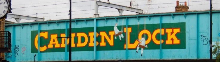 A blue bridge with 'Camden Lock' painted in yellow and two figures climbing painted on it.