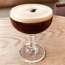 Espresso martini with a frothy top and coffee bean garnish on a wood table.