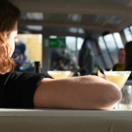 Two women sitting at a table with drinks on a sunlit boat.
