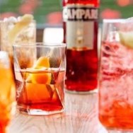 Assorted cocktails on a table with a bottle of Campari in the background.