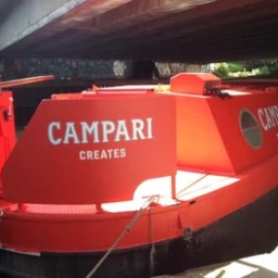 A red barge with 'Campari Creates' painted on the side under a bridge.