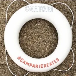 White lifebuoy on sand, marked 'CAMPARI' and '#CAMPARICREATES'.