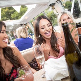 Three women laughing at a restaurant table with drinks and bottles.