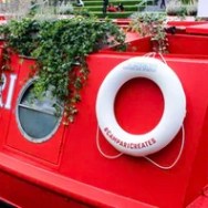 Red boat with round window, greenery, and life preserver labeled #camparicreates.
