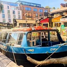 Blue canal boat docked beside modern urban buildings on a sunny day.