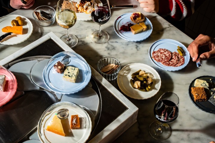 People enjoying wine and assorted cheese on a marble table.