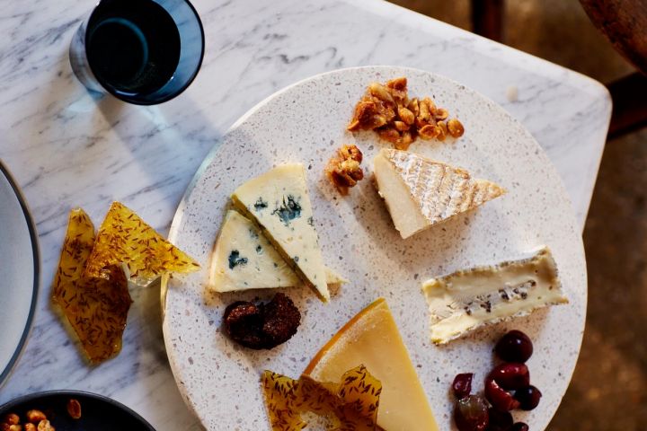 Assorted cheeses, grapes, and nuts on a speckled plate with a glass on a marble surface.
